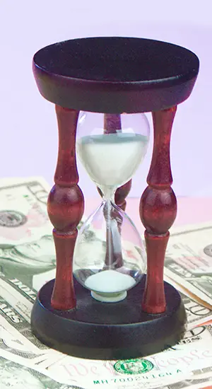 Hourglass sitting on scattered dollar bills, symbolizing how much time and money business owners lose managing their own bookkeeping instead of hiring a professional.